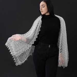 May include: A woman wearing a white lace shawl over a black turtleneck shirt and black jeans.