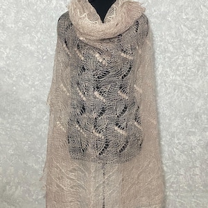May include: A delicate, light beige knitted shawl with a lacy pattern. The shawl is draped over a mannequin and has a flowing, ethereal look.