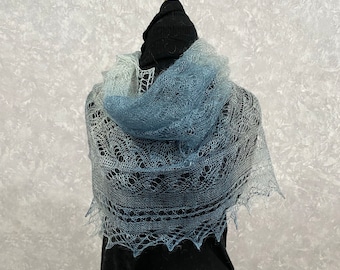 May include: A delicate, hand-knitted shawl in a gradient of blue and white. The shawl is made of a soft, lightweight yarn and features a delicate lace pattern.