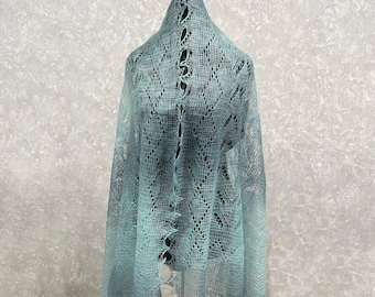 May include: A light blue lace shawl with a delicate pattern. The shawl is draped over a mannequin and has a slightly ombre effect.