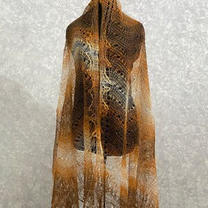 May include: A delicate brown and white lace shawl with a crocheted design. The shawl is draped over a mannequin and has a gradient of color from light to dark.