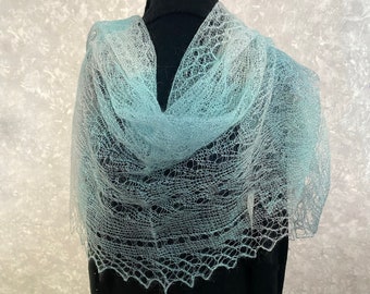 May include: A delicate, light blue lace shawl with a gradient effect, draped over a black mannequin.