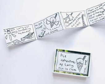May include: A small, handmade comic strip and a rectangular card. The comic strip, in black ink, depicts an ice cream cone named Larry sunbathing, dreaming of flying to Paris. The card reads "The Adventures of Larry the Ice Cream, Vol. One."