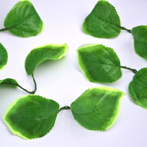 May include: A string of artificial green leaves with a light green border. The leaves are connected by thin wire stems.