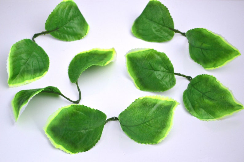 May include: A string of artificial green leaves with a light green border. The leaves are connected by thin wire stems.