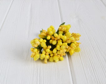 May include: A bunch of small, yellow, glittery flower buds with green stems. The buds are clustered together and have a slightly textured surface.