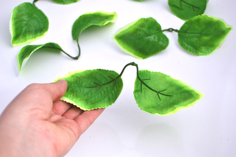May include: A collection of artificial green leaves with a light green border. The leaves are made of a soft, pliable material and have a realistic appearance.