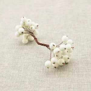 May include: A white berry spray with a brown wire stem. The berries are clustered together and have a fuzzy texture.