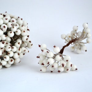 May include: Two bunches of white berry sprigs with brown wire stems. The berries are small and round with a slightly textured surface.