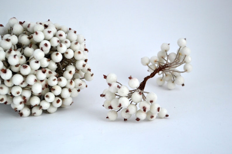 May include: Two bunches of white berry sprigs with brown wire stems. The berries are small and round with a slightly textured surface.