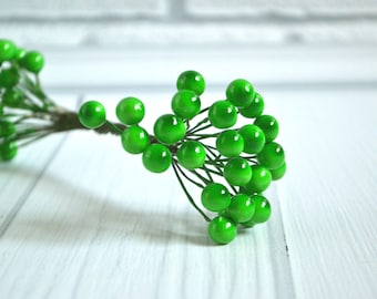 May include: A sprig of artificial green berries with a wire stem. The berries are clustered together in a bunch.