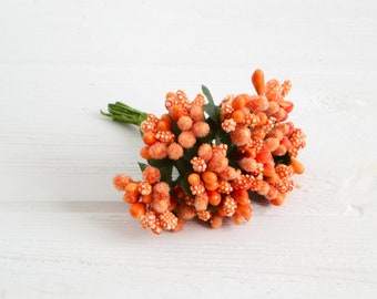 May include: A bunch of orange faux berry sprigs with green stems. The berries have a white speckled texture.