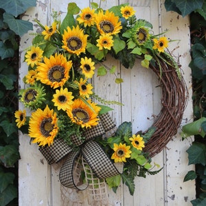 May include: A vibrant sunflower wreath with a rustic, natural grapevine base. The wreath features large, bright yellow sunflowers, green foliage, and a black and tan checkered bow. A decorative accent for doors or walls.