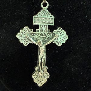 Könnte beinhalten: Ein Rosenkranz mit einem silberfarbenen Kruzifix und Verschluss. Das Kruzifix trägt die Inschrift "IESUS NAZARENUS REX IUDAEORUM". Der Rosenkranz hat geschnitzte beige Perlen und kleine rosa Perlen.