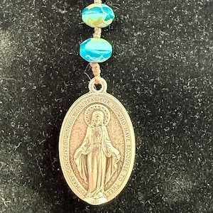 May include: A religious keychain featuring a silver-tone clasp, three turquoise beads, and a pendant with an image of the Virgin Mary. The pendant has the inscription "O Mary conceived without sin pray for us who have recourse to thee."