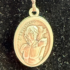 Könnte beinhalten: Ein Schlüsselanhänger mit silbernem Verschluss und rundem Anhänger. Der Anhänger hat drei facettierte blaue Perlen, die durch goldfarbene Perlen getrennt sind. Der Anhänger zeigt das Bild einer Person.