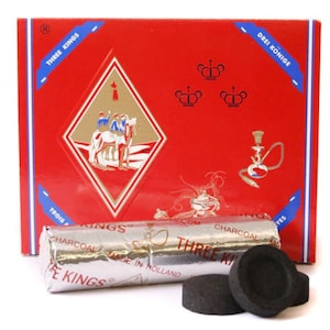 May include: A box of Three Kings charcoal briquettes for hookah, with a red box featuring a diamond-shaped logo with three kings on horseback. The box also has the text "Three Kings" and "Drei Könige" on it. The charcoal briquettes are wrapped in silver foil and have the text "Three Kings Charcoal Made in Holland" on them.