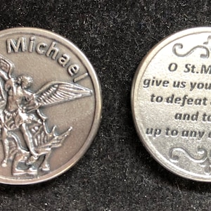 May include: A silver-toned metal coin with an image of Saint Michael slaying a dragon on one side and a prayer to Saint Michael on the other side. The prayer reads: "O St. Michael give us your strength to defeat our fears and to rise up to any challenge."