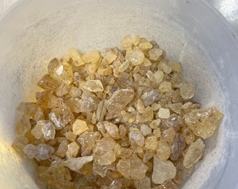 Op de afbeelding: Een witte kom gevuld met kleine, doorschijnende, amberkleurige harsstukjes.