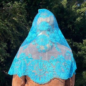 May include: A light blue lace mantilla with a floral design. The mantilla is made of a sheer fabric and has a scalloped edge.