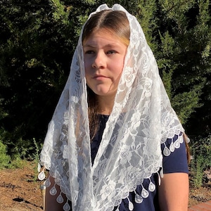 May include: White lace mantilla with a floral pattern and scalloped edges. The mantilla has a beaded fringe with teardrop-shaped beads.