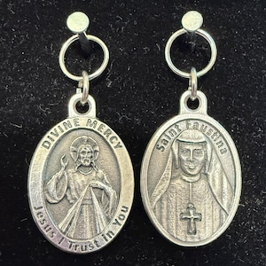 Puede incluir: Dos colgantes ovalados plateados. Uno presenta a Jesús con el texto "Divina Misericordia" y "Jesús, confío en ti". El otro representa a Santa Faustina con el texto "Santa Faustina."