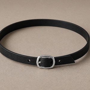 Pode incluir: Um cinto de couro preto com uma fivela prateada. O cinto &eacute; circular e parece ser projetado para ser usado ao redor do pesco&ccedil;o. A fivela &eacute; retangular e tem um design simples e cl&aacute;ssico. Circunfer&ecirc;ncia de cerca de 45 cm.