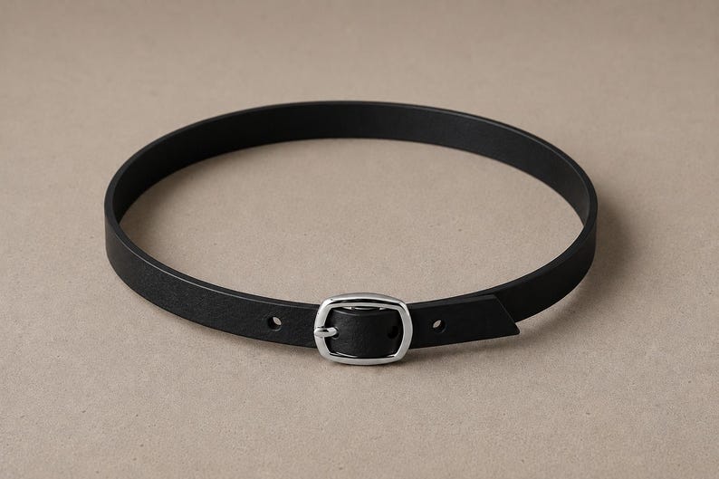 Pode incluir: Um cinto de couro preto com uma fivela prateada. O cinto &eacute; circular e parece ser projetado para ser usado ao redor do pesco&ccedil;o. A fivela &eacute; retangular e tem um design simples e cl&aacute;ssico. Circunfer&ecirc;ncia de cerca de 45 cm.
