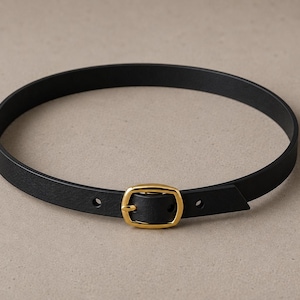 Pode incluir: Um cinto de couro preto com uma fivela dourada. O cinto &eacute; circular e parece ser feito de um material liso. A fivela &eacute; retangular com bordas arredondadas.