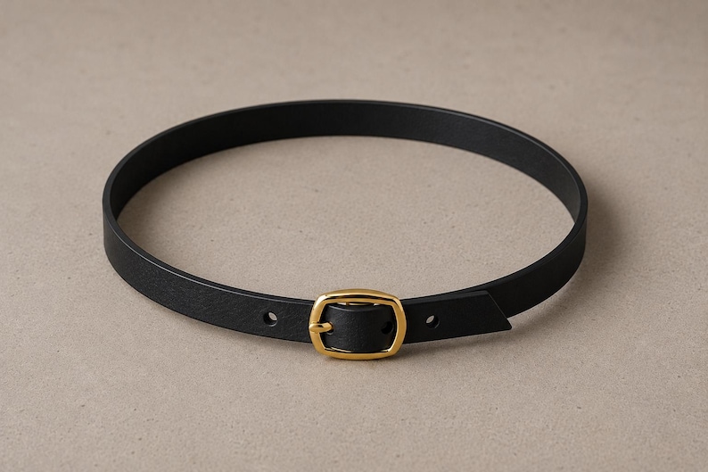 Pode incluir: Um cinto de couro preto com uma fivela dourada. O cinto &eacute; circular e parece ser feito de um material liso. A fivela &eacute; retangular com bordas arredondadas.