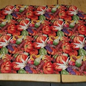 May include: A black fabric table runner with a fall harvest theme. The runner is covered in a repeating pattern of gourds, pumpkins, and corn. The runner has a scalloped edge and is sewn with a black thread.