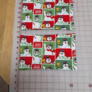 May include: Two red and green fabric pot holders with a repeating pattern of Frosty the Snowman. The pot holders are approximately 7 inches by 5 inches.