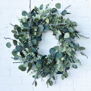 Artificial wreath made of mixed eucalyptus and lavender sprigs hanging on a white brick wall