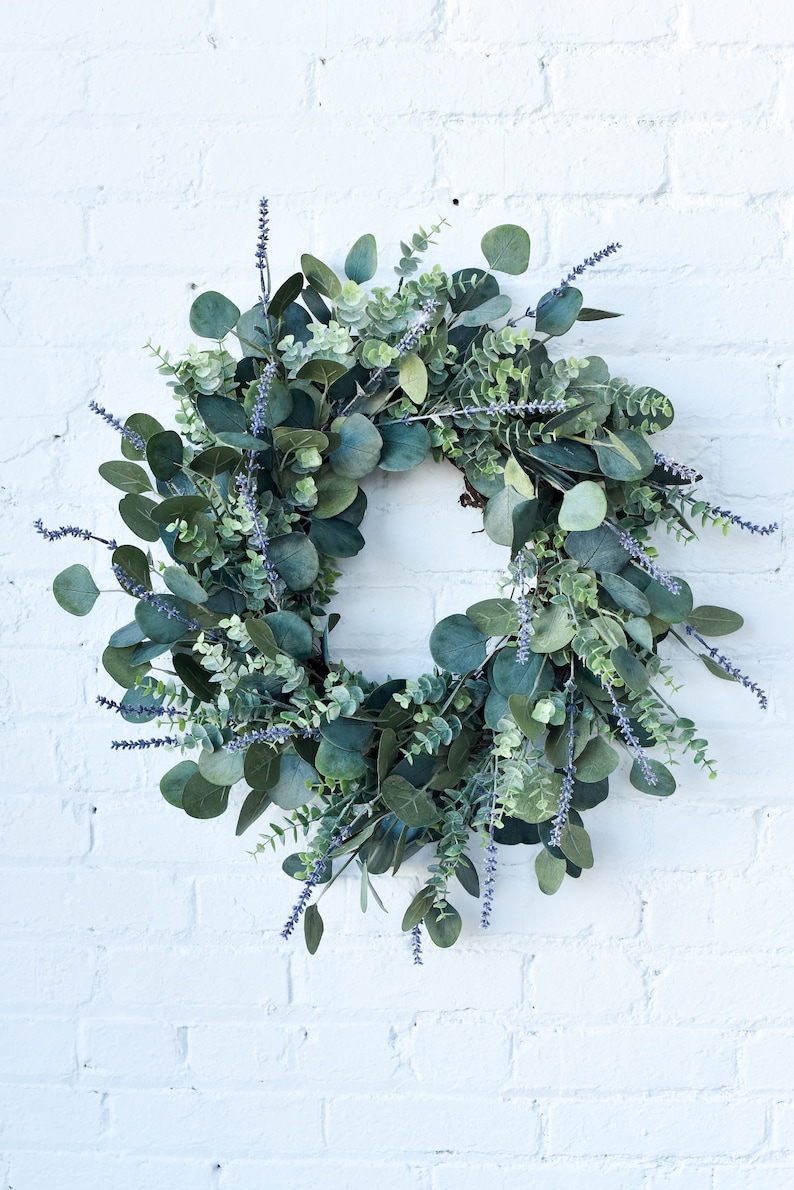 Artificial wreath made of mixed eucalyptus and lavender sprigs hanging on a white brick wall