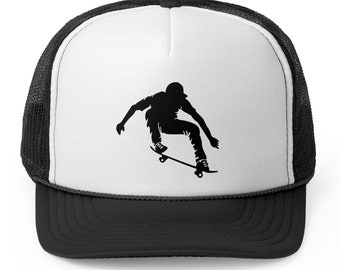Peut inclure: Une casquette de camionneur noire et blanche avec une silhouette d'une personne faisant du skateboard sur le devant. La casquette a un dos en maille noire et un devant blanc.