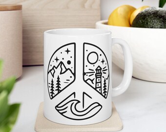 Peut inclure: Une tasse en céramique blanche avec une illustration en noir et blanc d'un symbole de paix. Le symbole de paix est divisé en trois sections, chacune représentant une scène différente : des montagnes, un phare et des vagues.