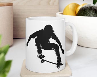 Peut inclure: Une tasse en céramique blanche avec une silhouette noire d'une personne faisant du skateboard. La tasse a une poignée sur le côté droit.