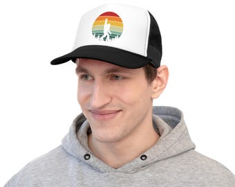 Peut inclure: Une casquette de camionneur noire et blanche avec un graphique de coucher de soleil rétro représentant une silhouette de Bigfoot levant le bras en l'air. La casquette a un dos en maille noire.
