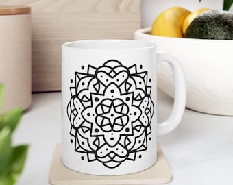 Peut inclure: Une tasse en céramique blanche avec un motif mandala noir et blanc. La tasse a une anse et est posée sur un dessous de tasse.