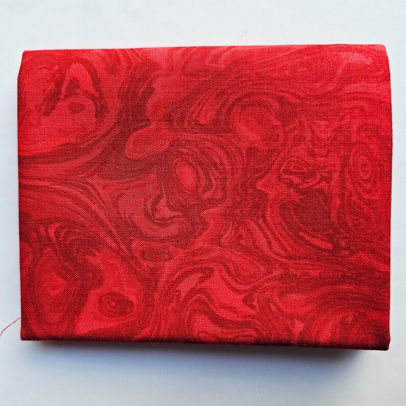 Op de afbeelding: Een rechthoekig, rood stoffen item met een wervelend, gemarmerd patroon in verschillende tinten rood. De stof lijkt strak geweven en de randen zijn netjes afgewerkt. De algemene indruk is van een decoratief of functioneel textiel.