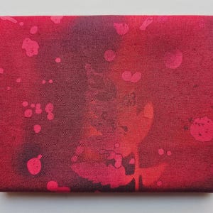 Op de afbeelding: Een rechthoekig stuk stof in rood- en donkerroodtinten. Het heeft een spetterpatroon in roze en rood. De textuur van de stof is zichtbaar, wat het ontwerp verdiept. Een opvallend, artistiek textiel.