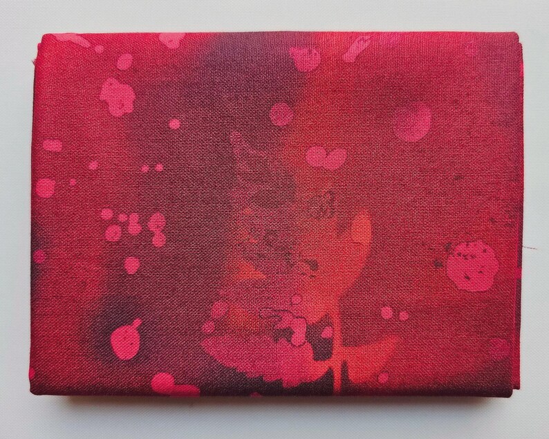 Op de afbeelding: Een rechthoekig stuk stof in rood- en donkerroodtinten. Het heeft een spetterpatroon in roze en rood. De textuur van de stof is zichtbaar, wat het ontwerp verdiept. Een opvallend, artistiek textiel.