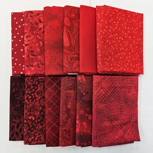 May include: A collection of folded fabric squares in various shades of red. The fabrics display diverse patterns, including polka dots, floral designs, and abstract textures. The color palette ranges from deep burgundy to bright crimson, suitable for quilting or crafting projects.