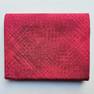 Op de afbeelding: Een rechthoekig, gevouwen stoffen item in een dieprode kleur, met een subtiel, donker kruispatroon. De textuur lijkt enigszins ruw, met een matte afwerking. Het item is waarschijnlijk een portemonnee of een kleine etui.