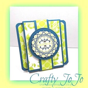 Può includere: Un biglietto di auguri con motivo blu-verde e verde con un design circolare bianco e giallo al centro. Il biglietto è piegato a metà e ha un bordo decorativo.