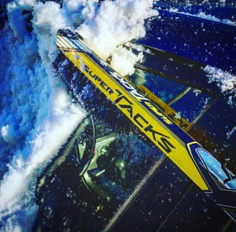 May include: A yellow and blue hockey stick with the text "SUPER TACKS" printed on it. The stick is partially covered in snow.