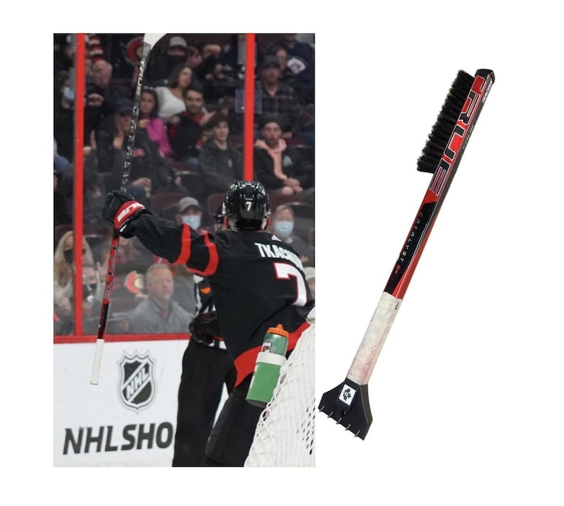 May include: A red and black ice hockey stick with a black brush on the end. The stick has the word "TRUE" printed on it in white letters. The brush is made of black bristles and is attached to the stick with a black metal handle.