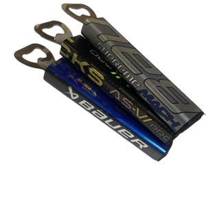 May include: Three hockey stick bottle openers. The top opener is gray with the text "Supreme Mach" and "Pro". The middle opener is black with the text "CKS" and "AS-V". The bottom opener is blue with the text "Bauer".