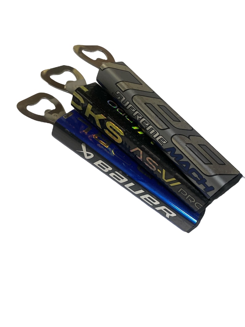 May include: Three hockey stick bottle openers. The top opener is gray with the text "Supreme Mach" and "Pro". The middle opener is black with the text "CKS" and "AS-V". The bottom opener is blue with the text "Bauer".