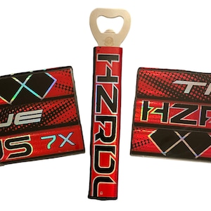 May include: Red and black hockey-themed bottle opener with a silver bottle opener. The bottle opener has the text "HNZR" on it. The two coasters have the text "JS 7X" and "TF HZR" on them.